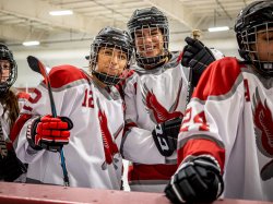 Women's hockey players in uniform pose for photo on the ice near the boards