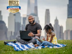 adult student holding laptop sitting next to their child on a picnic blanket