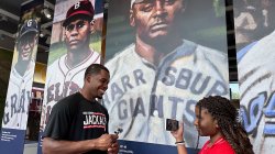 A young reporter interviews a New Jersey Jackals baseball player in front of a display featuring historical baseball players at the Hinchliffe Stadium exhibit.