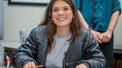Transfer student Abigail Rodriguez sits at a desk inside a classroom with a notebook in front of her and holding a pencil.