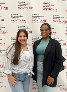 Two women standing in front of a white branded backdrop. Both are smiling and happy.