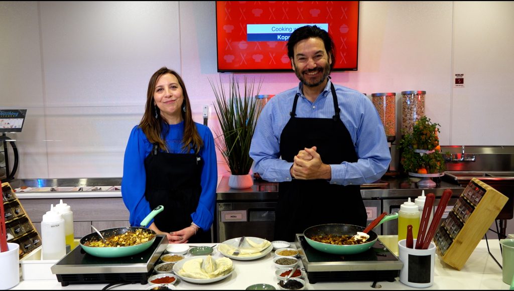 A woman on the left and a man on the right, both standing in front of a stove. Both are smiling and happy.