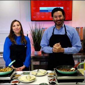 A woman on the left and a man on the right, both standing in front of a stove. Both are smiling and happy.